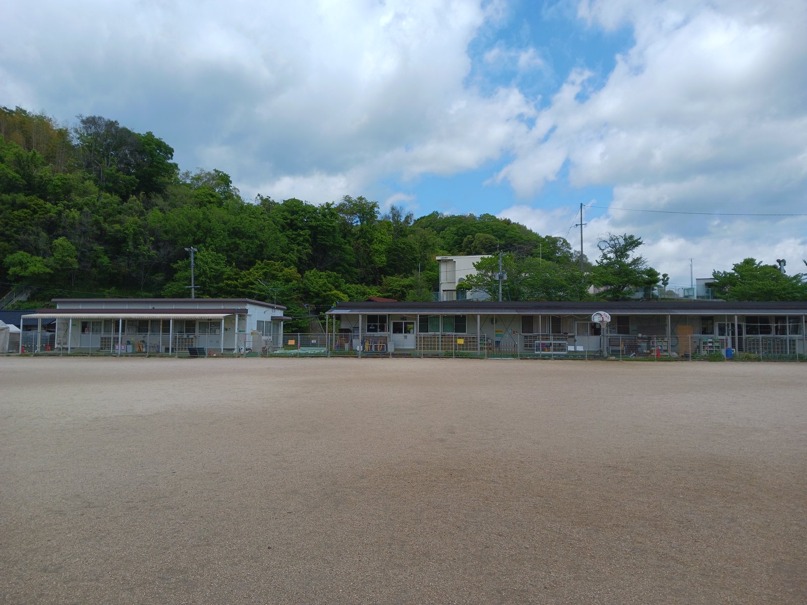 校庭ごしに見えるながおキッZ児童クラブの建物。奥は緑の山と空