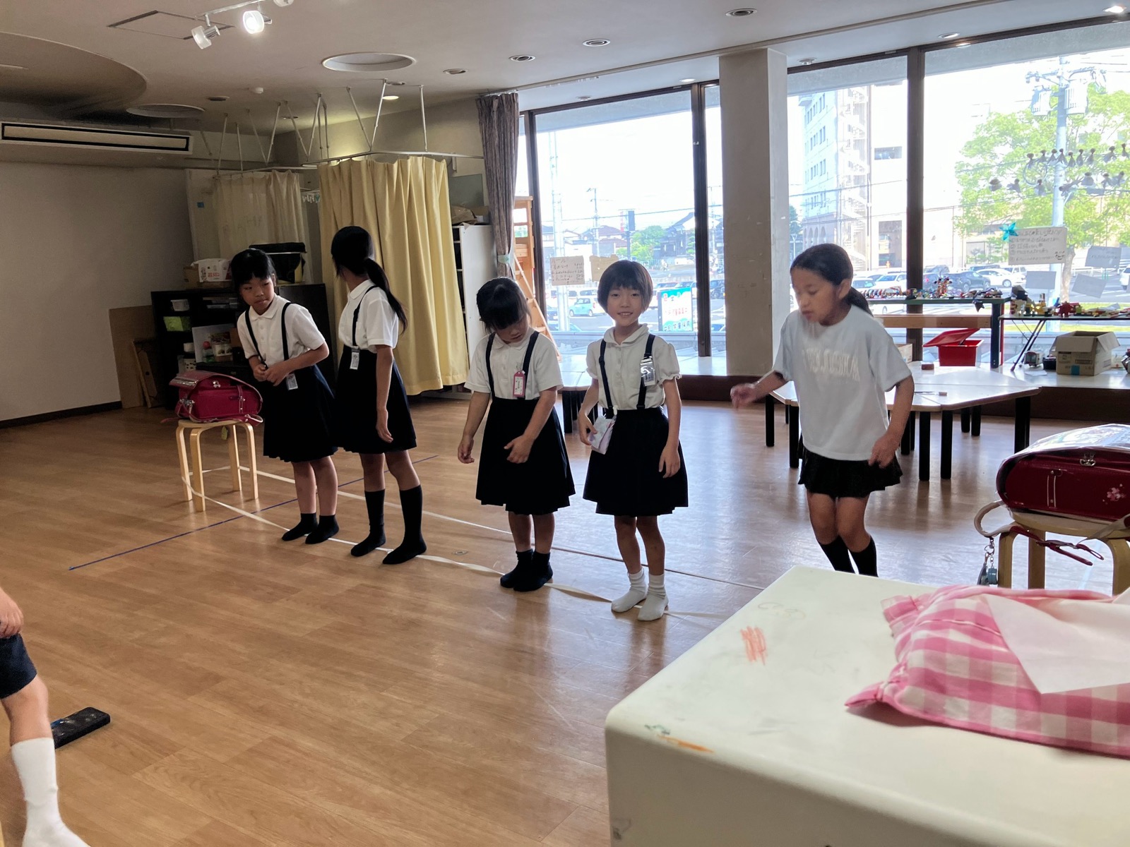 制服姿のこどもたちが、床に張ったテープの線に沿って並んで立っている様子
