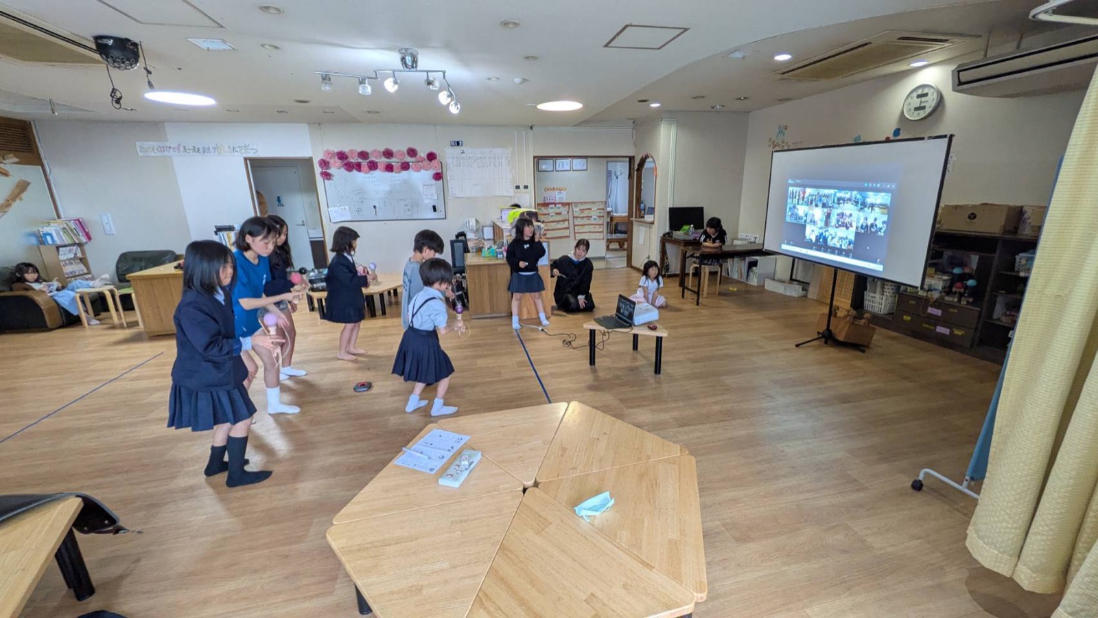 スクリーンにオンラインの画面が映る部屋で、こどもたちがけん玉をしている様子