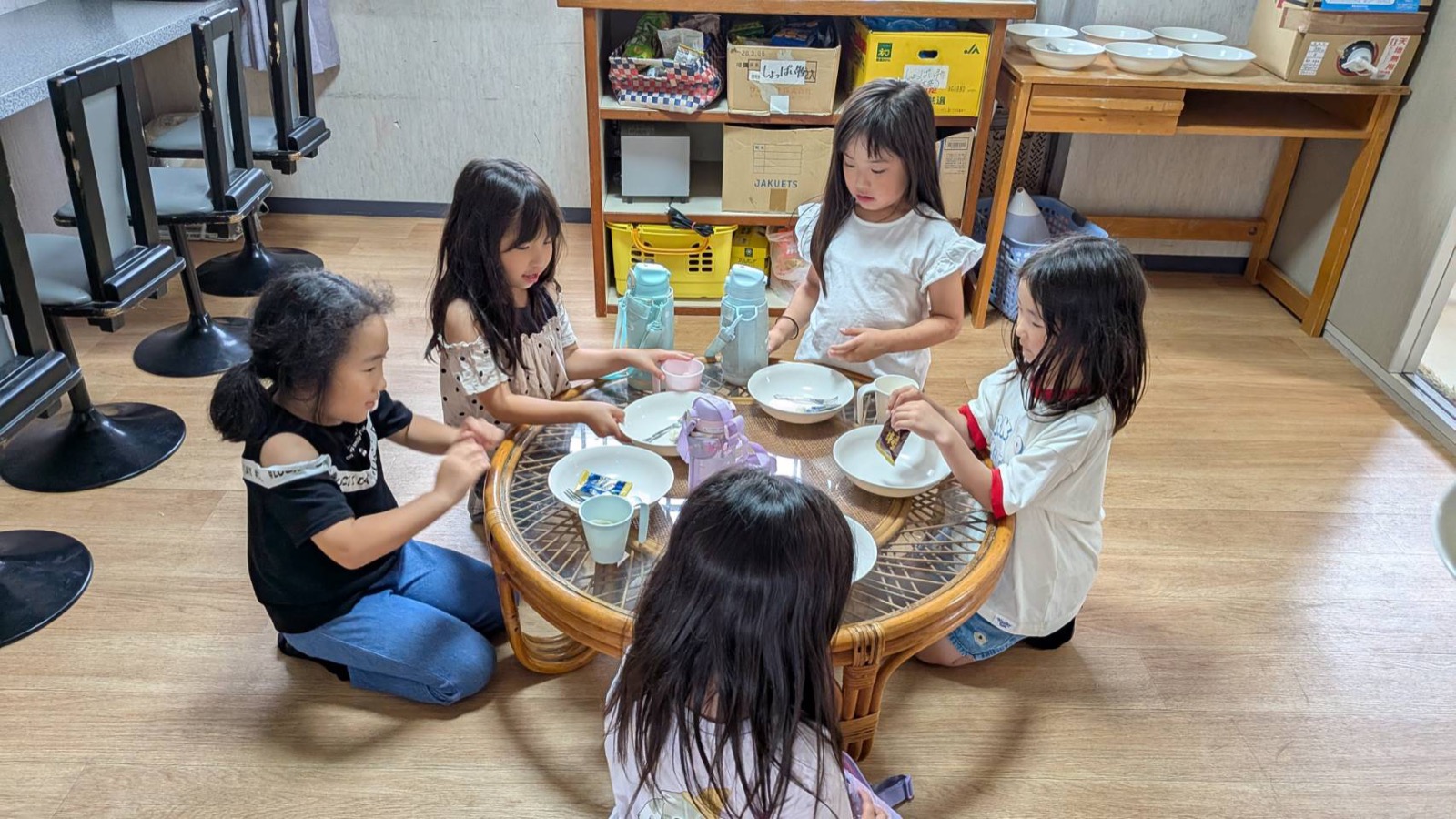 こどもたちが丸いテーブルを囲んで座り、器を並べておやつの用意をしている様子