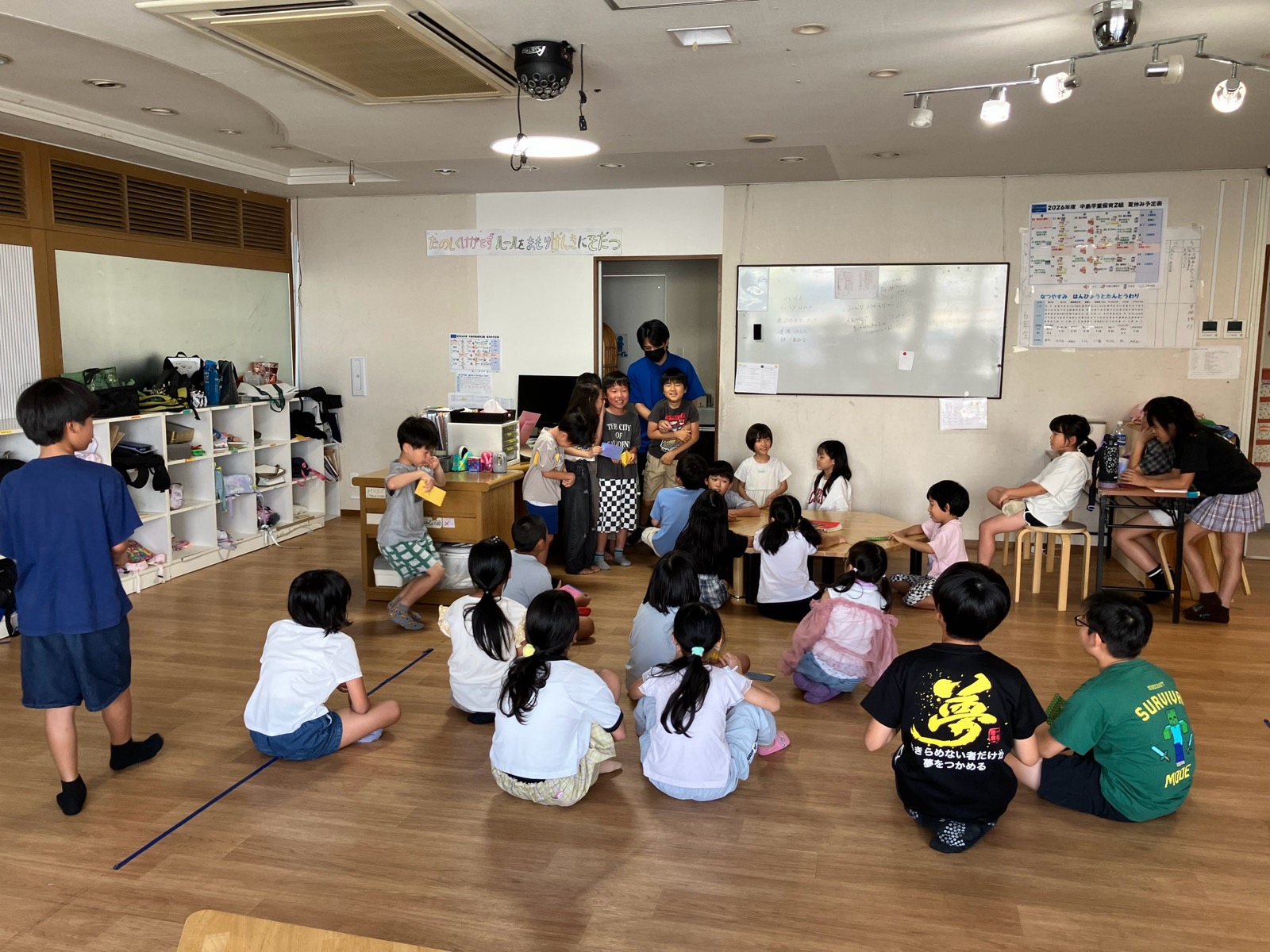 床に座ったこどもたちが、前に立つ友だちと支援員のほうを見ている様子