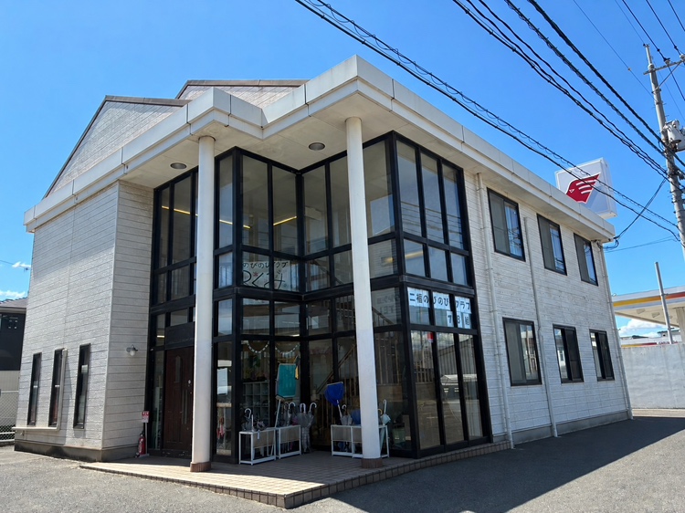 白い2階建ての建物。角が総ガラス張りで、入口の上に「二福のびのびクラブ」の看板がかかっている