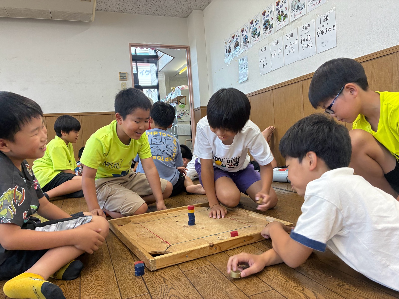 床に座ったこどもたちが、木の盤を囲んでカロムをして笑っている様子