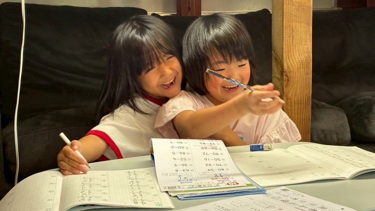 二人のこどもが、並んで宿題をしながら笑い合っている様子
