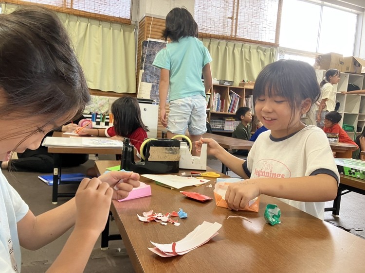 こどもたちが机で、折り紙や紙を使って工作をしている様子